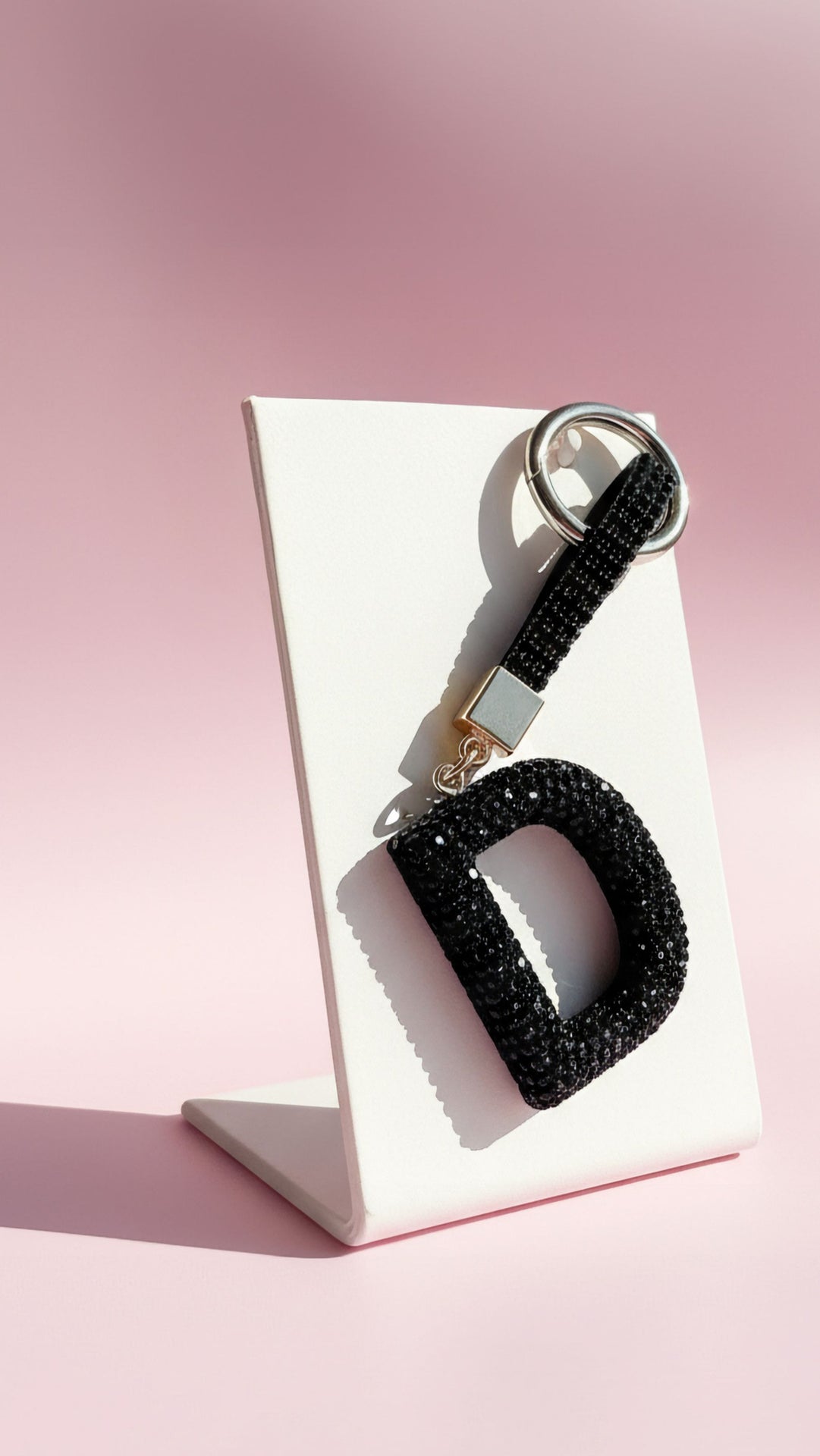 Black letter 'D' keychain with glittery texture on a pink background