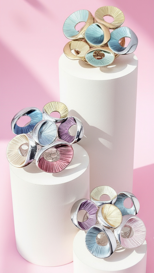 Colorful circular brooches on white cylindrical stands against a pink background