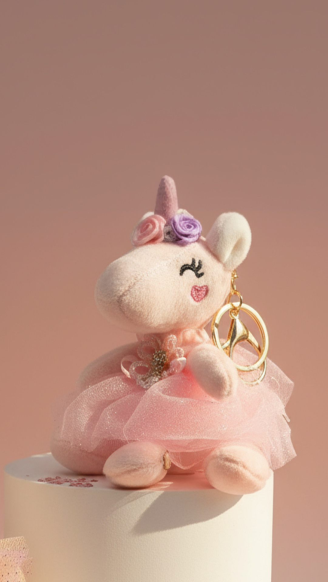 Unicorn-shaped plush keychain with pink dress and rose on a beige background