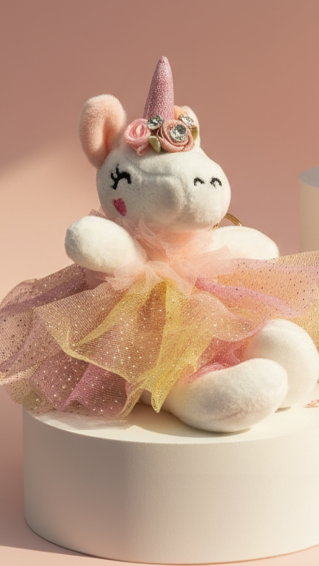 Plush unicorn keychain with a pink dress and horn on a beige background