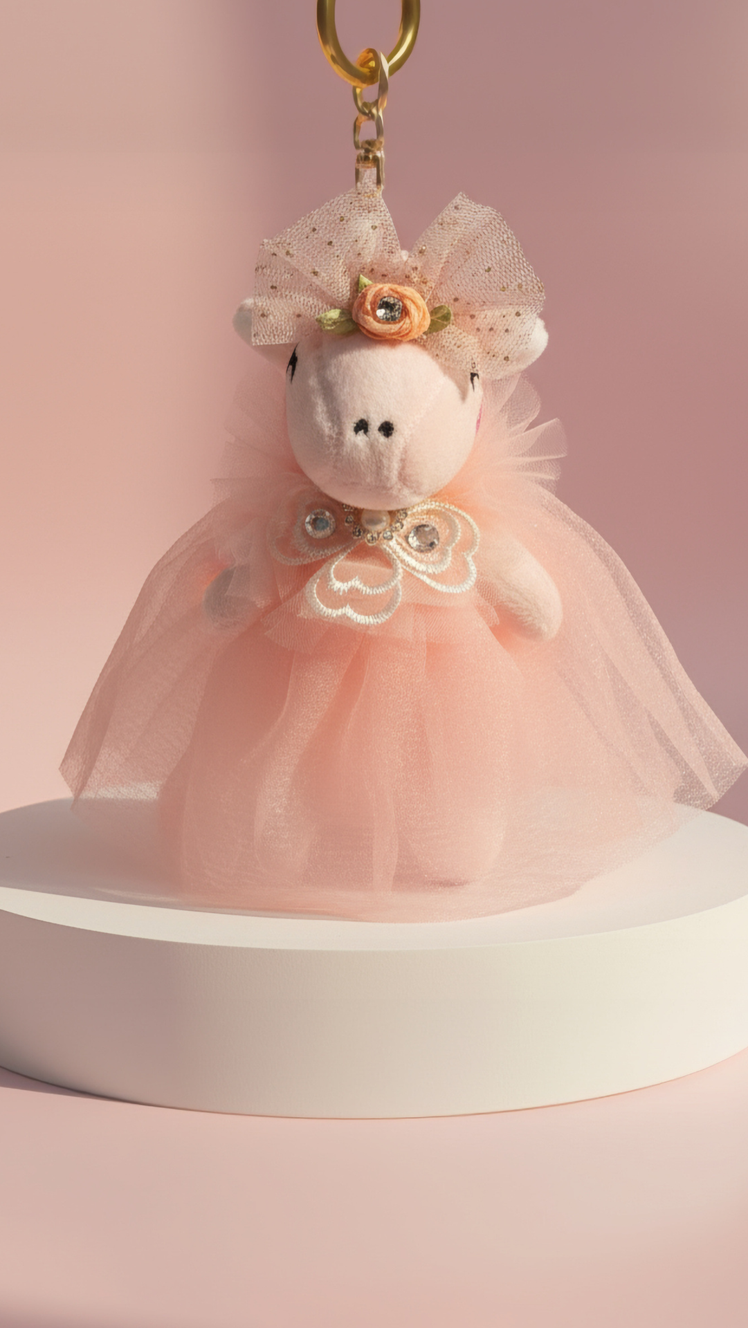 Stuffed animal keychain in a pink dress with a bow on a pink background
