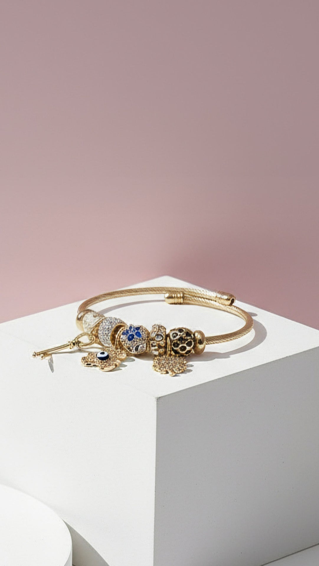 Evil eye golden bracelet displayed on a pink background and white base