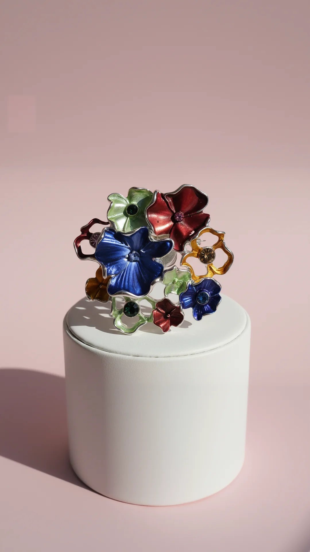 Multicolor decorative floral brooch, displayed against a pink background.