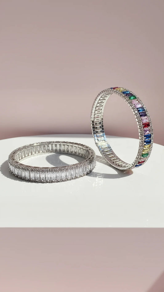 Two bracelets with gemstones on a white surface with a pink background