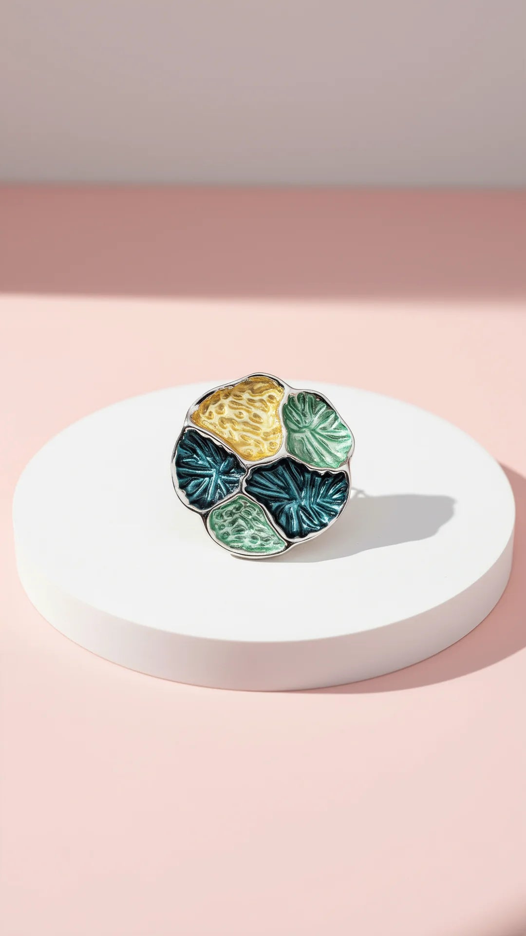 colorful brooch displayed on a white display against a pink background